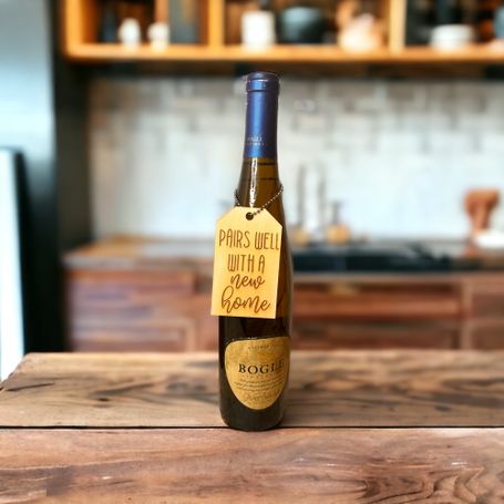 a laser engraved wine bottle tag that says pairs well with a new home on bottle of wine in a kitchen